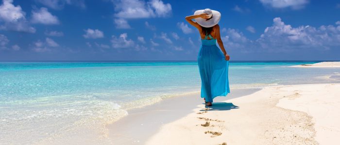 Frau im blauem Kleid läuft an einem tropischen Strand und genießt ihren Urlaub